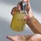 Hand holding a bottle of Dermalogica conditioning hand and body wash with clear liquid being poured.
