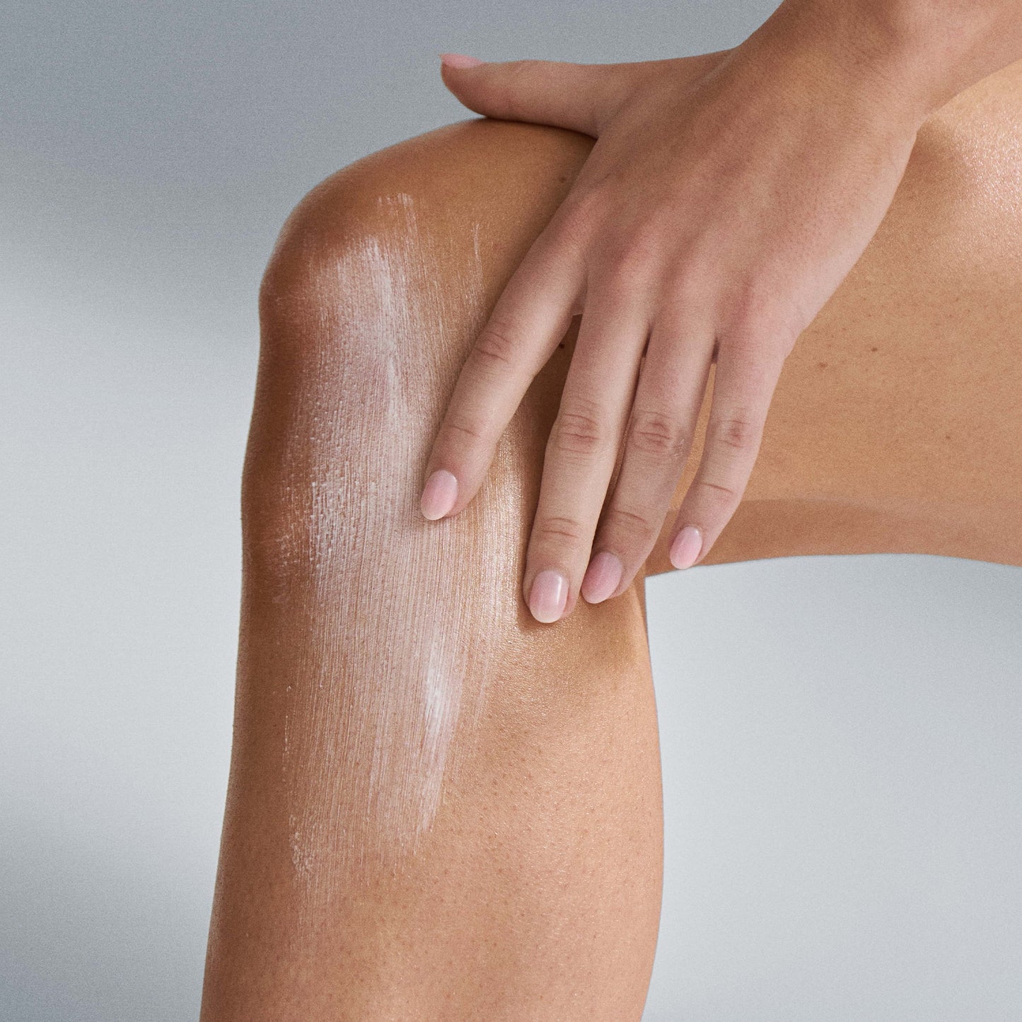 Person applying a white cream(protection 50 sport SPF) to their knee with a neutral background 